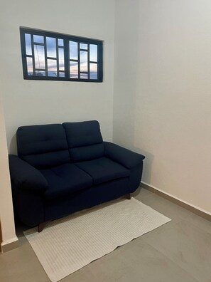 Ein dunkelblaues Sofa vor einer weißen Wand, darüber ein Fenster.