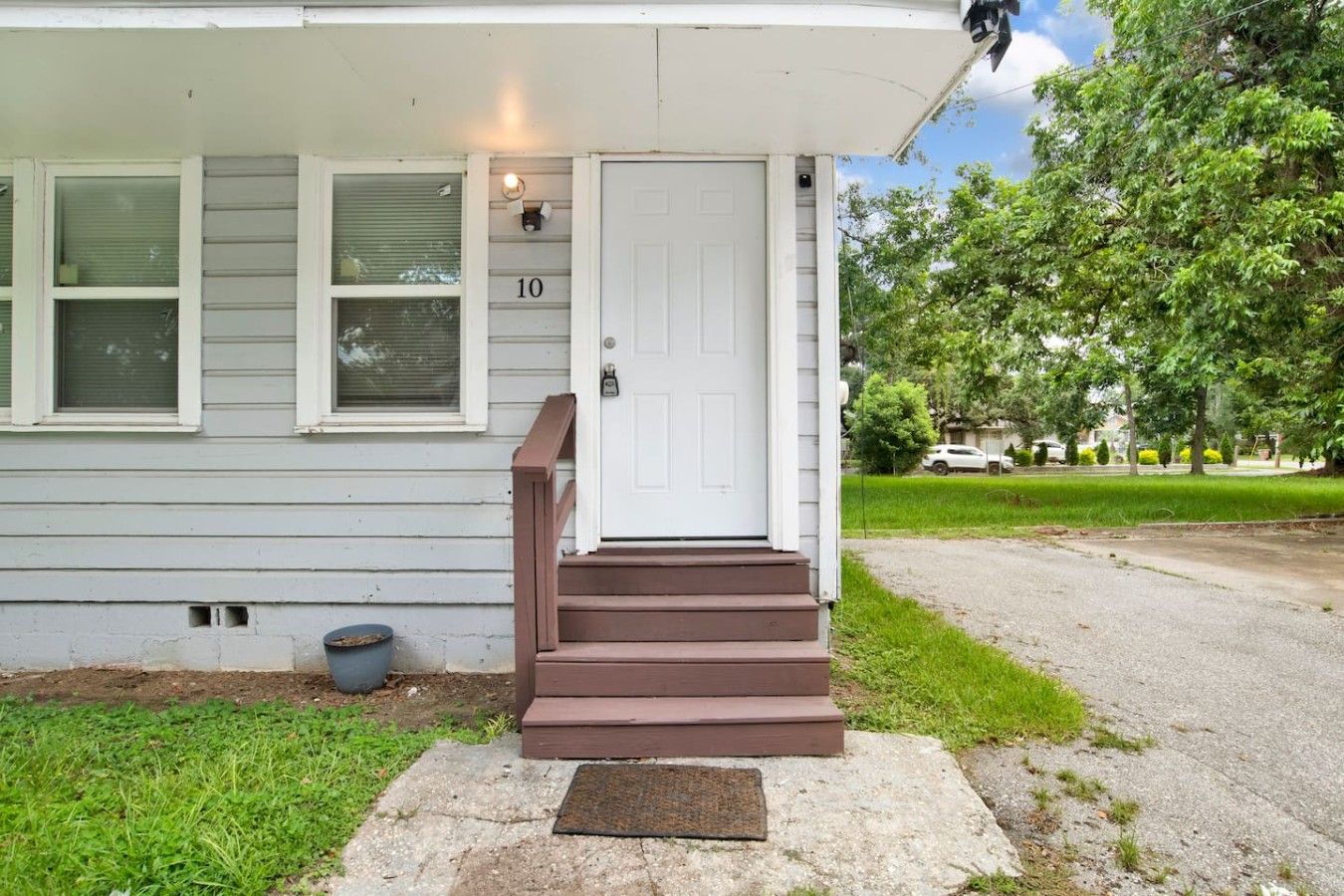 Uma casa residencial com porta branca, um conjunto de degraus marrons levando à entrada e uma caixa de correio no chão.
