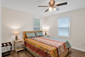 A bedroom with a bed, two bedside tables, a chair, a ceiling fan, and two windows with blinds. - Michigan in Mobile (Mobile)