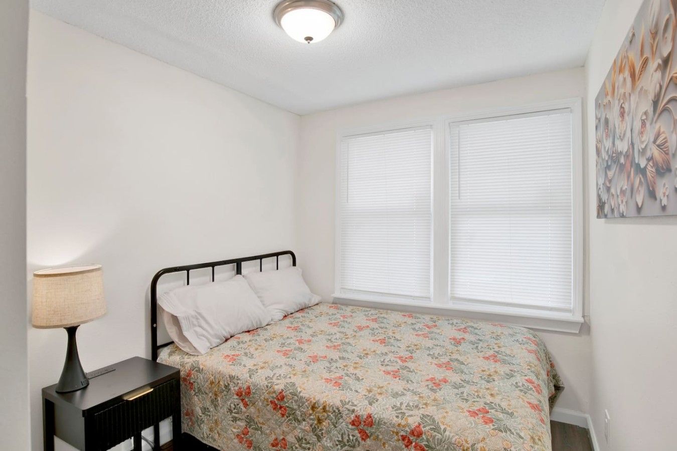 Une chambre à coucher avec un lit, une table de chevet, une lampe et une fenêtre avec des stores.