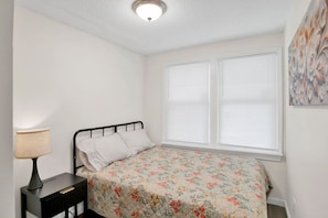 A bedroom with a bed, a nightstand, a lamp, and a window with blinds. - Michigan in Mobile (Mobile)