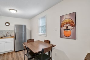 A kitchen with a refrigerator, a dining table with chairs, a window with blinds, and a wall-mounted picture. - Michigan in Mobile (Mobile)