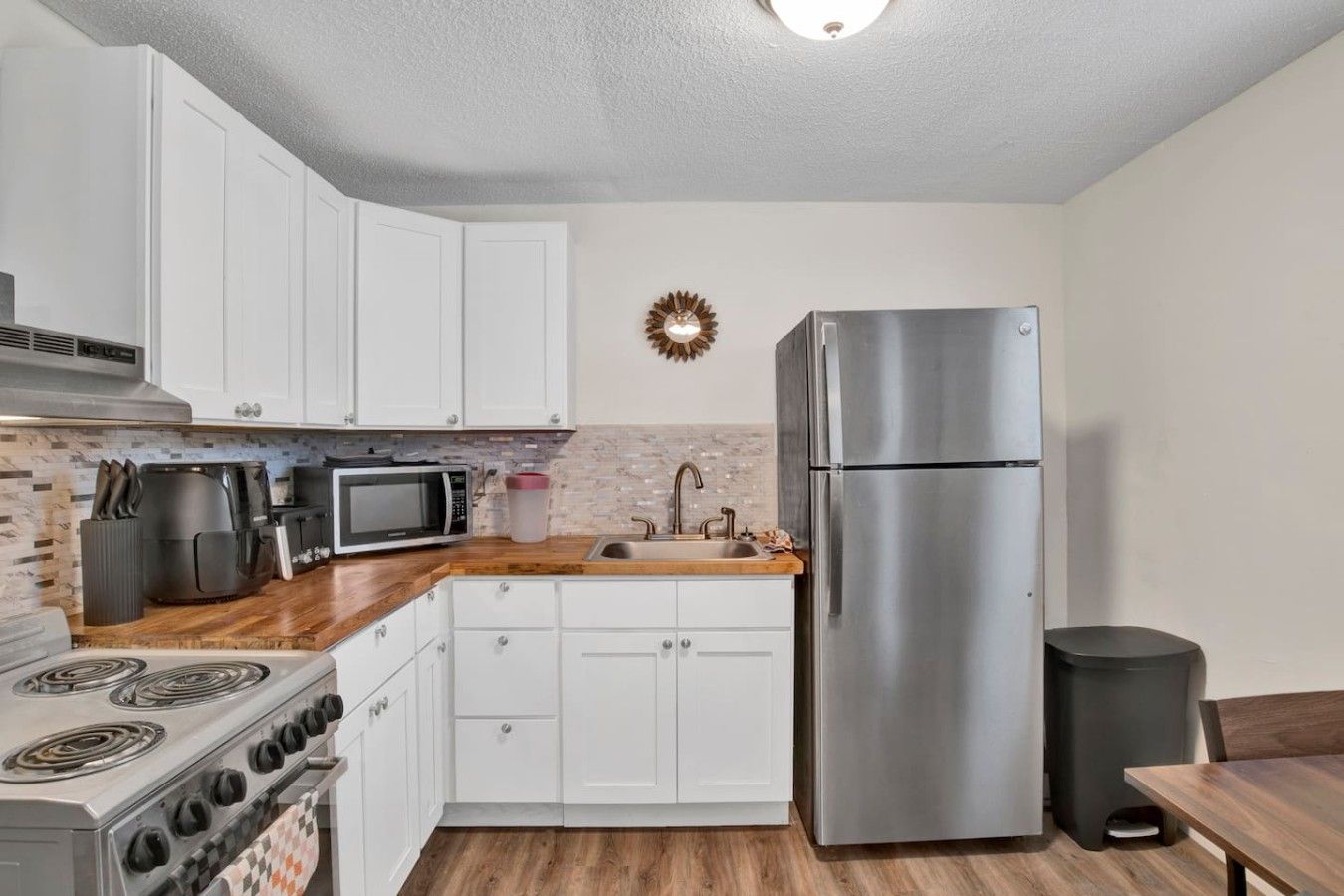 A compact kitchen with white cabinets, a stainless steel refrigerator, a microwave, a stove, and a sink.