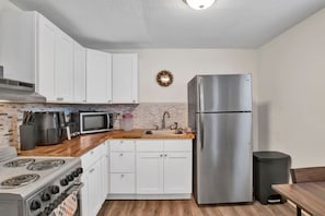 A compact kitchen with white cabinets, a stainless steel refrigerator, a microwave, a stove, and a sink. - Michigan in Mobile (Mobile)