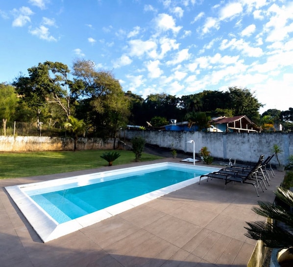 Una piscina rectangular amb una terrassa enrajolada, envoltada per una paret baixa i una zona verda.