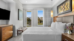 Habitación de hotel con una cama grande, televisor, escritorio y vistas al exterior.