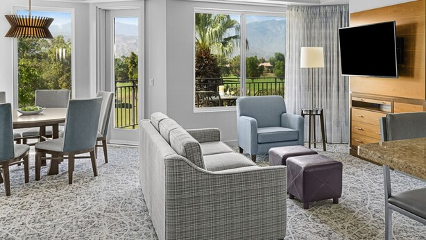 A modern hotel room with a dining area, a sofa set, a TV, and a view of the outdoors. - Marriott Vacation Club- large 2 bd 2ba unit (Palm Desert)