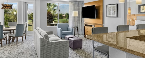 Habitación de hotel moderna con comedor, sofá, televisor y vistas al exterior.