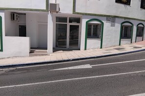 Um edifício com fachada branca, entrada por porta de vidro e calçada de azulejos.