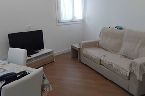 Ein Wohnzimmer mit Flachbildfernseher auf einem Schrank, einem beigen Sofa und einem kleinen Tisch.