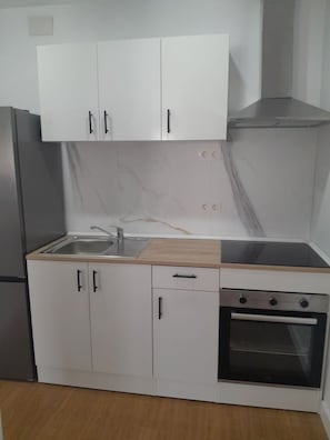 Eine Küche mit weißen Schränken, einem Edelstahlkühlschrank, einer Spüle, einer Holzarbeitsplatte und einem Backofen.
