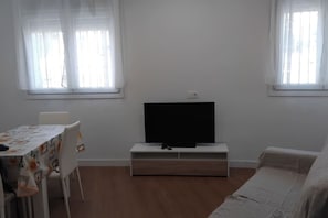 A room with a flat-screen TV on a white stand, a dining table with chairs, and a sofa. - Blue Summer An Apartment (Nerja)