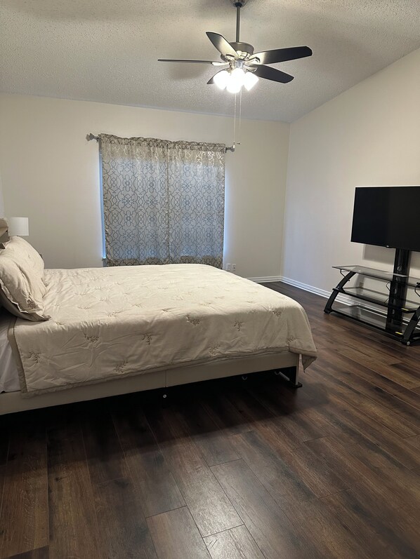A bedroom with a bed, a ceiling fan, a television on a stand, and a window with curtains.