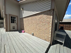 A wooden deck with a brick wall, a door, and a metal bench.