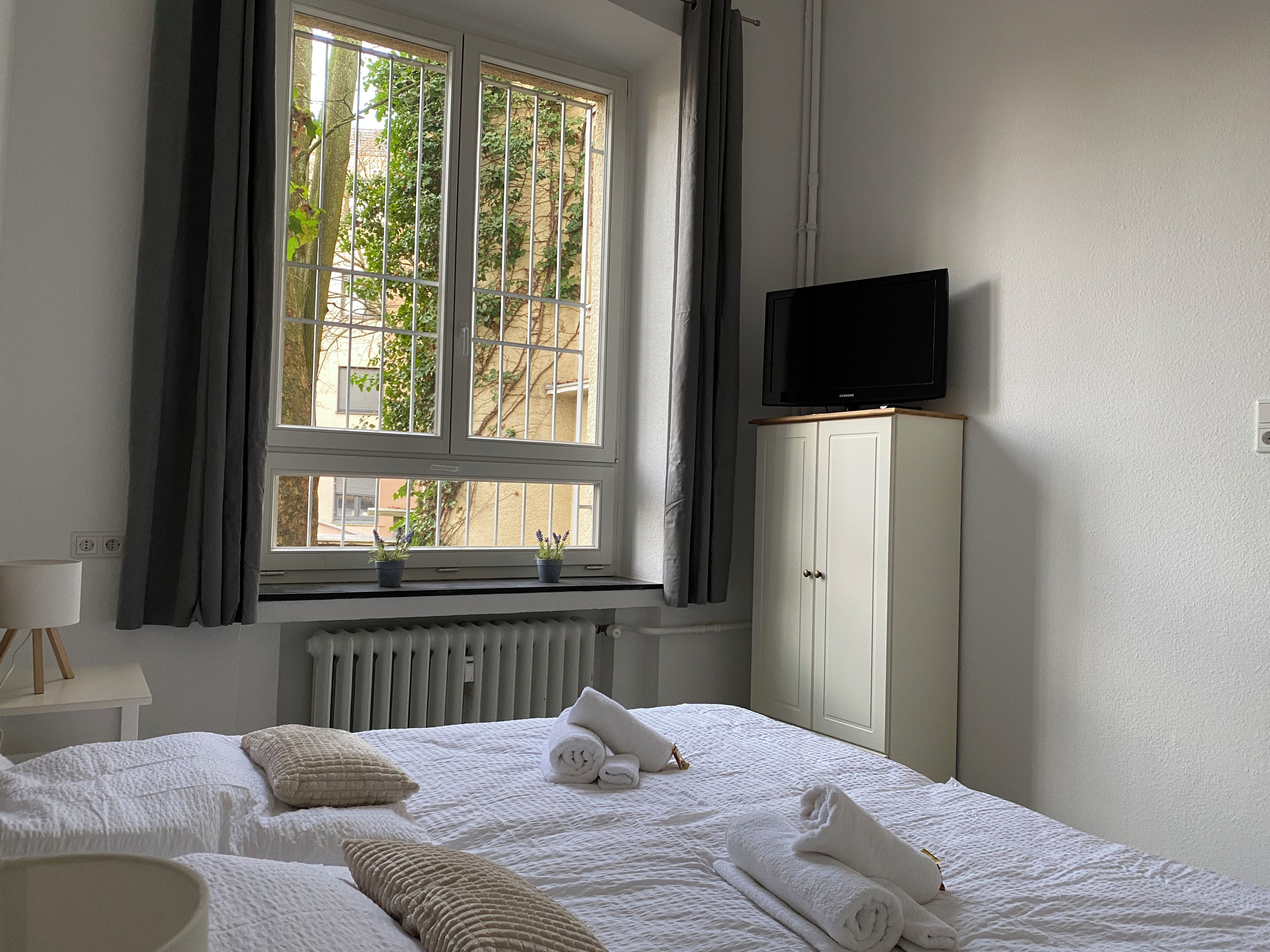 Ein Hotelzimmer mit Bett, Fernseher, Schrank und einem Fenster mit Vorhängen.