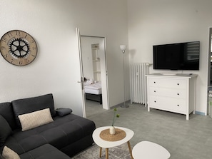 Ein modernes Hotelzimmer mit einer schwarzen Couch, einem weißen Schminktisch, einem Flachbildfernseher und einer Holz-Wanduhr.
