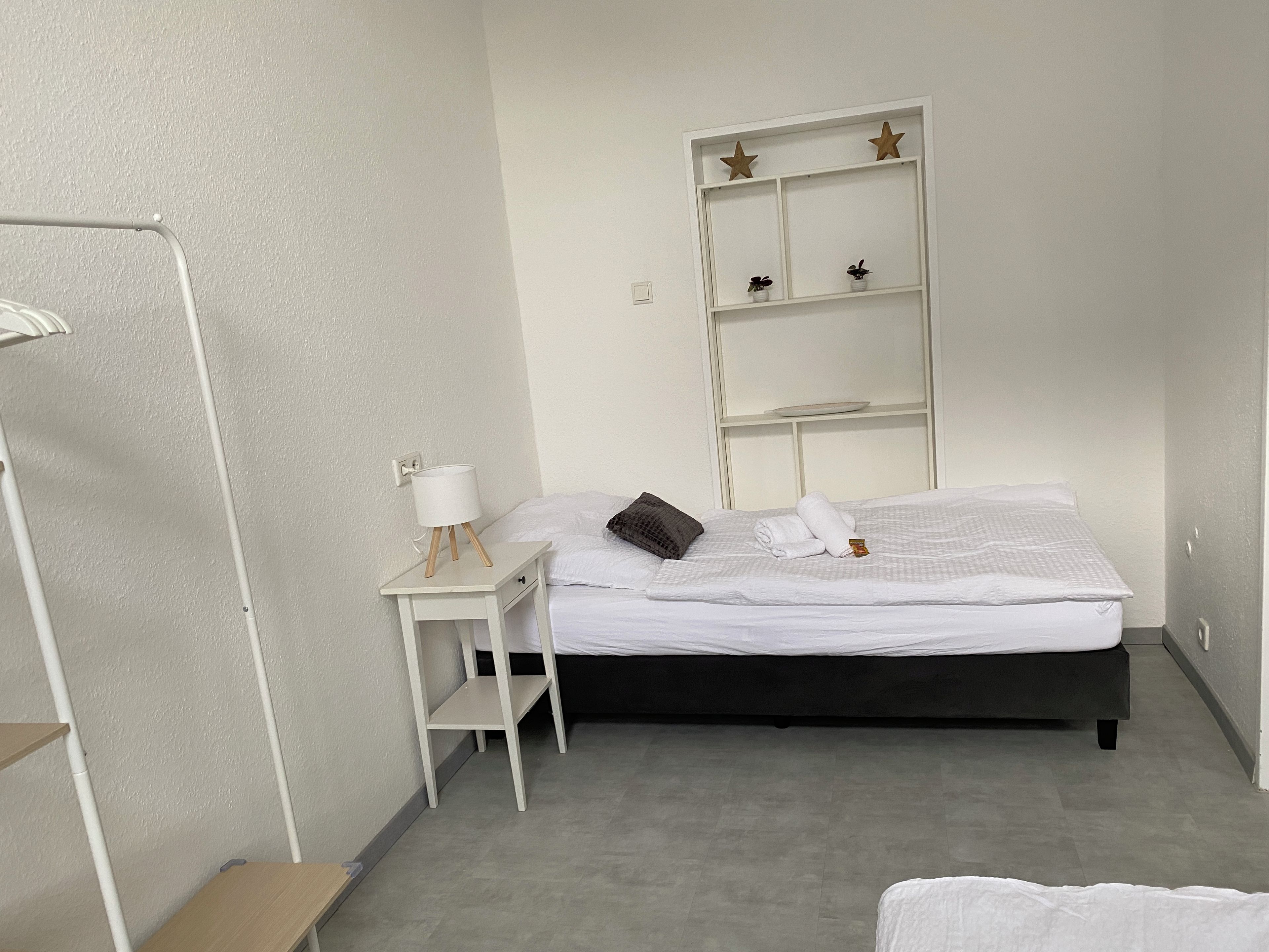 Ein ordentlich eingerichtetes Hotelzimmer mit einem Bett, einem Nachttisch mit Lampe, einem Regal mit Dekoration und einem Kleiderschrank.