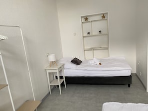Ein ordentlich eingerichtetes Hotelzimmer mit einem Bett, einem Nachttisch mit Lampe, einem Regal mit Dekoration und einem Kleiderschrank.
