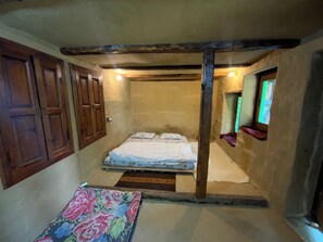 A small, rustic bedroom with a single bed, wooden beams on the ceiling, and a window with a view. - Tranquil 1-bedroom Mud House in charming Bashisht perfect for getaway (Bashisht)