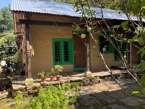 A rustic building with a corrugated metal roof, a wooden door, and a green window. - Tranquil 1-bedroom Mud House in charming Bashisht perfect for getaway (Bashisht)