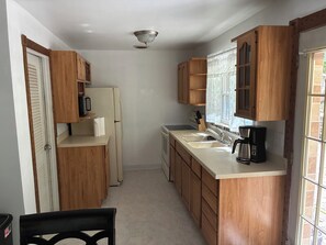 Eine kleine Küche mit Holzausstattung, inklusive Kühlschrank, Kaffeemaschine und einem Fenster mit Vorhängen.