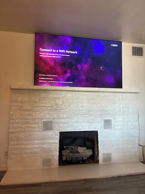 A flat-screen TV mounted above a white brick fireplace with a starry sky wallpaper. - Cozy Family-Friendly 2-Bedroom Lakeview Retreat in Waverly, OH with AC (Waverly)