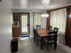 A dining area with a wooden table and chairs, a kitchen with cabinets, and a door leading outside. - Cozy Family-Friendly 2-Bedroom Lakeview Retreat in Waverly, OH with AC (Waverly)
