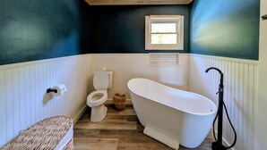 Een badkamer met een houten plafond, een wit bad, een toilet en een raam.