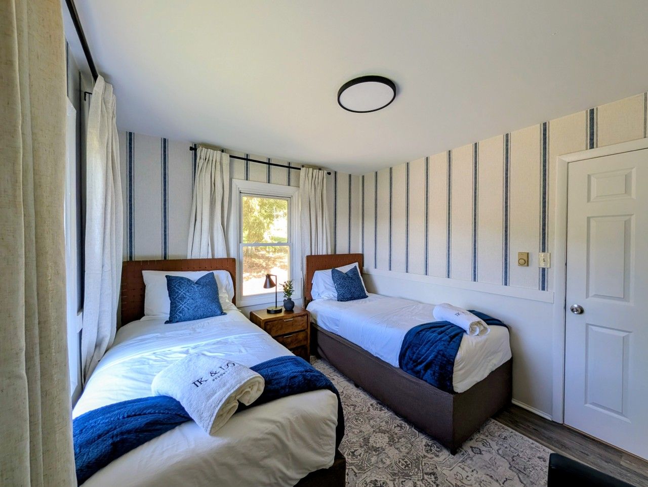 A double room with two beds, a window, a door, and a small bedside table.