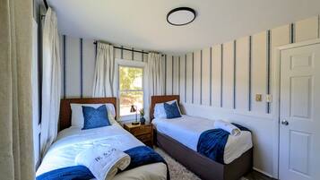 A double room with two beds, a window, a door, and a small bedside table.