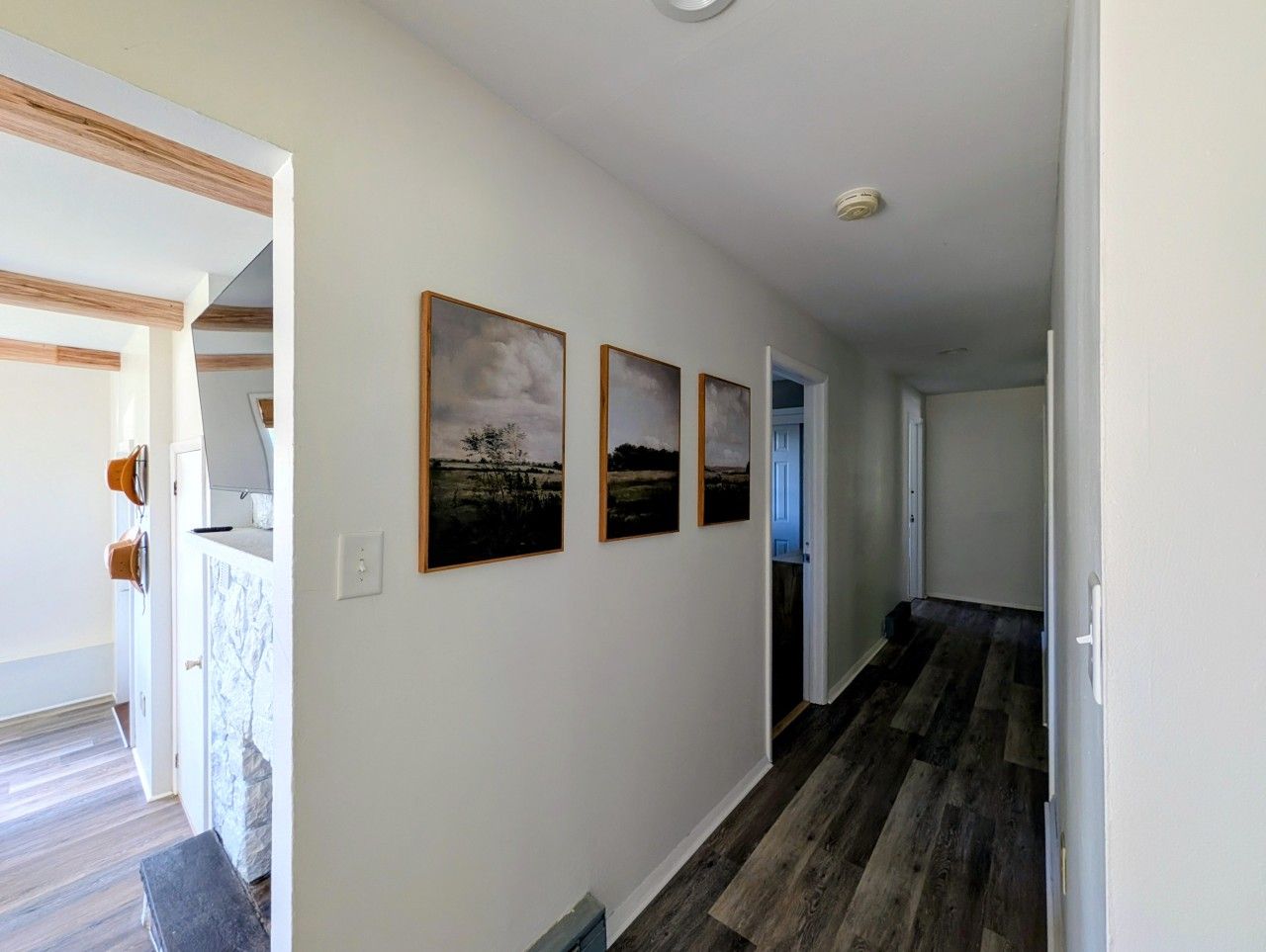A hallway with wooden flooring, white walls, and three framed pictures.