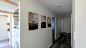 A hallway with wooden flooring, white walls, and three framed pictures.
