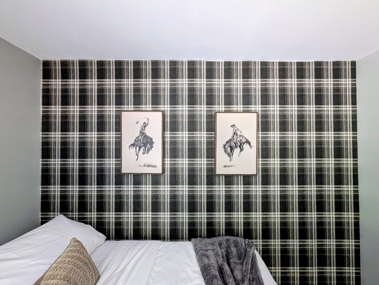 A bedroom with a plaid wallpaper, a bed with white bedding, and two framed pictures on the wall.