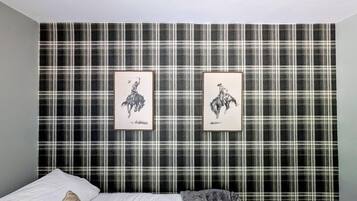 A bedroom with a plaid wallpaper, a bed with white bedding, and two framed pictures on the wall.