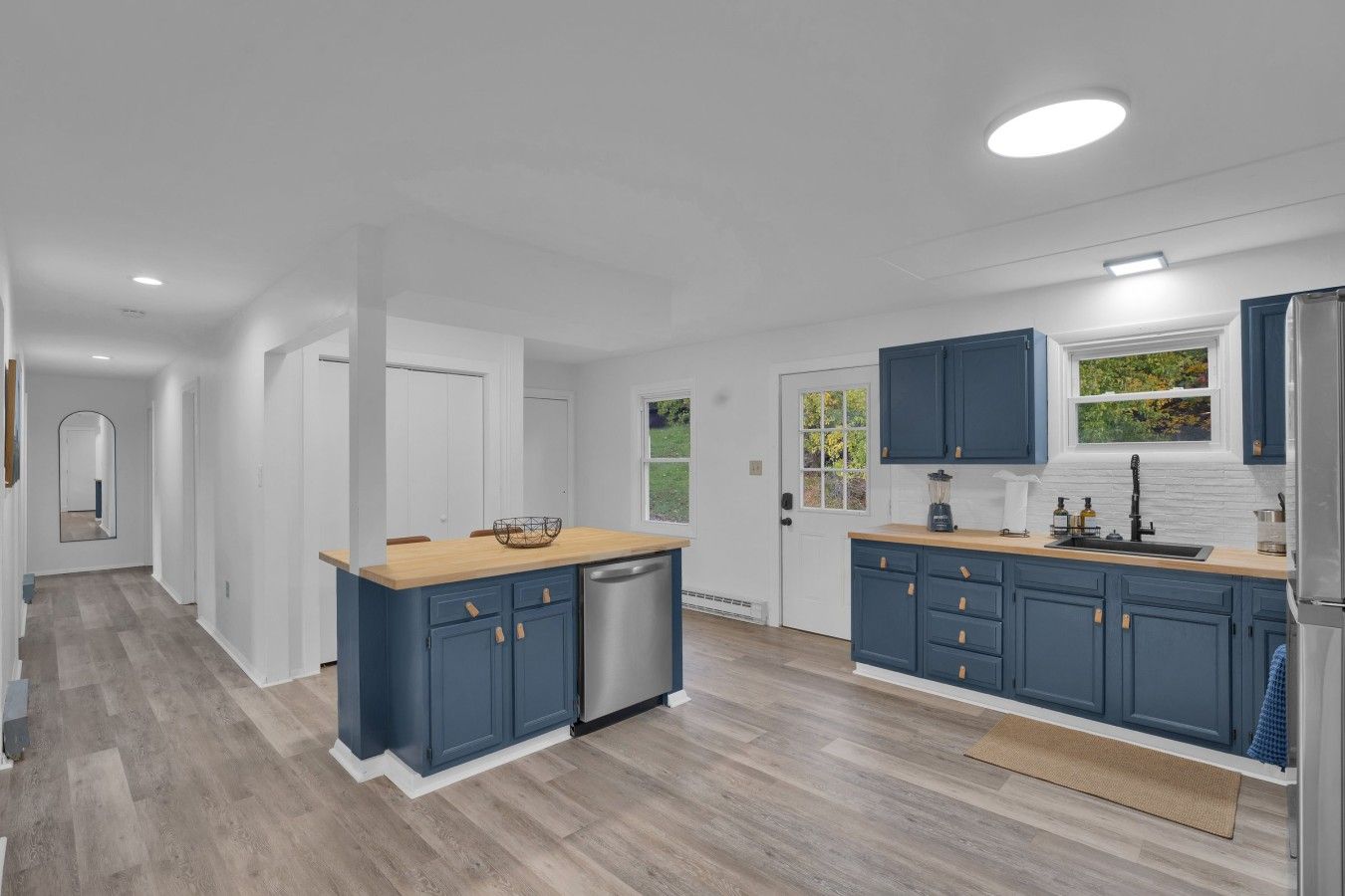 Una cocina moderna con piso de madera, paredes blancas y gabinetes azules.
