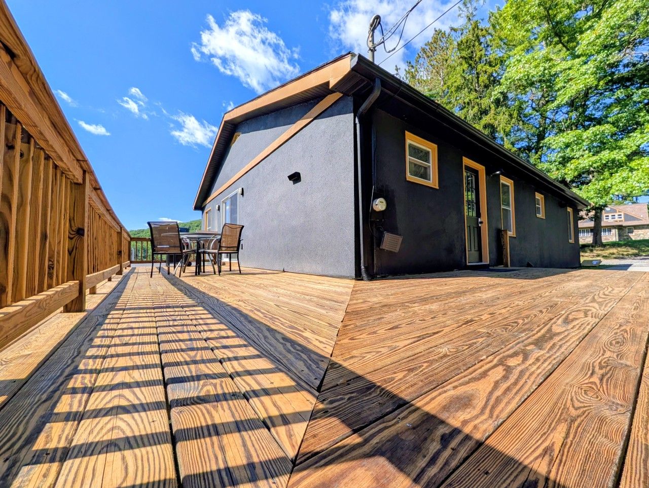 A wooden deck leading to a building with a dark facade and yellow trim windows.