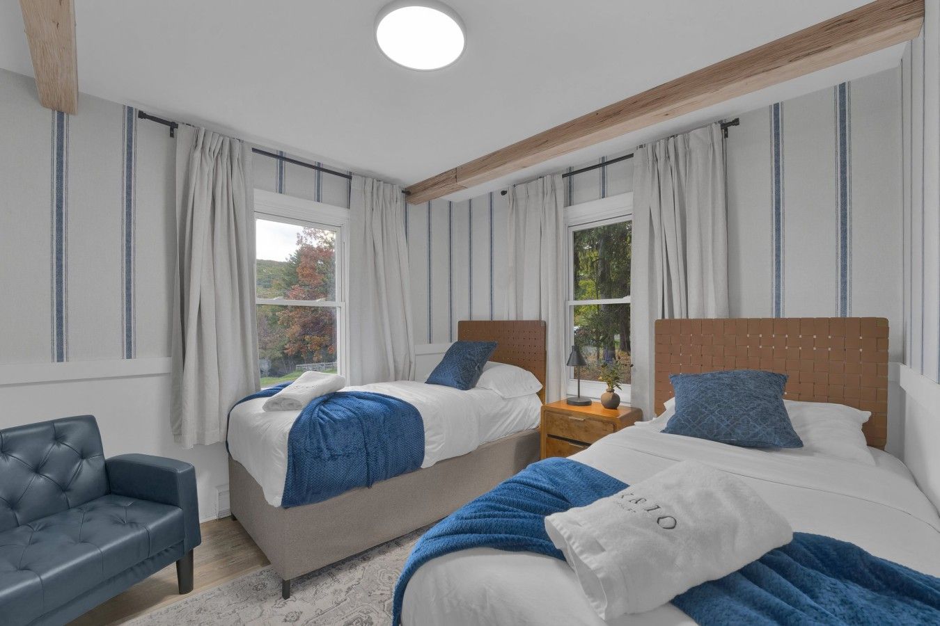 Habitación doble con dos camas, un sofá gris y una ventana con cortinas.