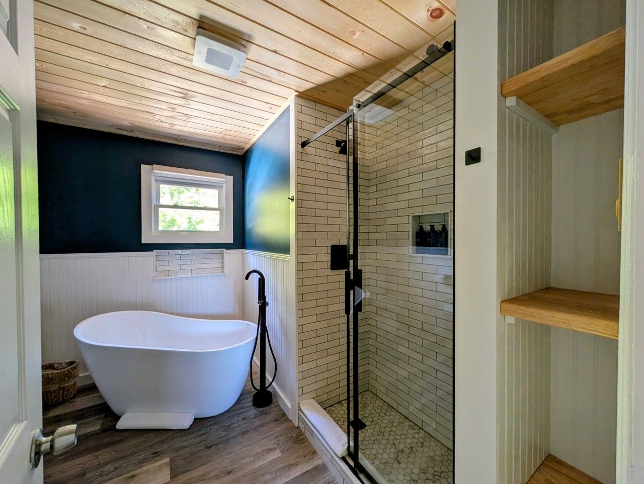 A bathroom with a freestanding bathtub, a glass-enclosed shower, and a window providing natural light.