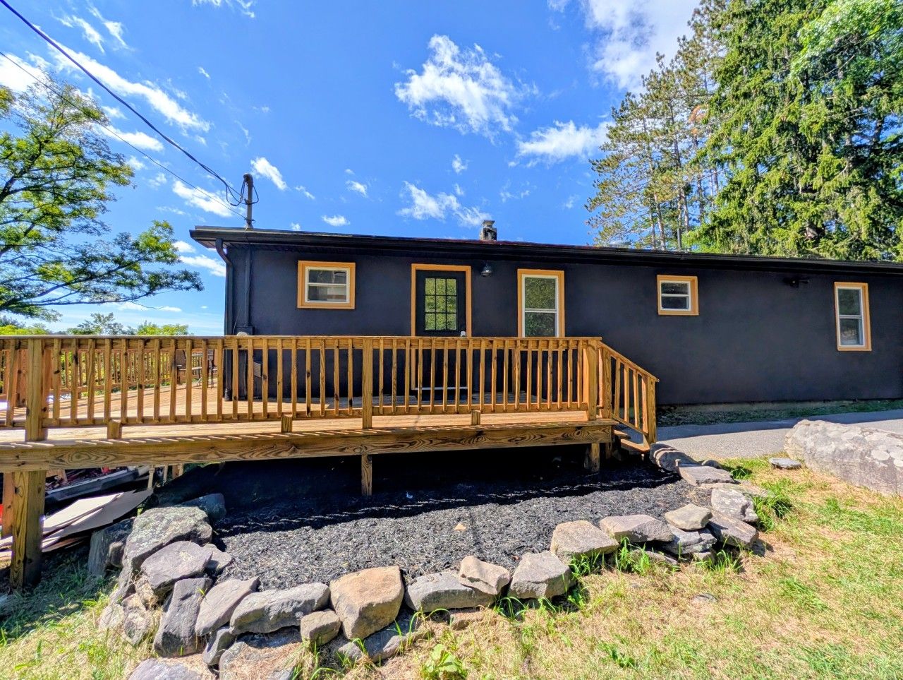 Un bâtiment à deux étages doté d’une terrasse en bois et d’un chemin de pierre menant à l’entrée.