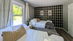 Een slaapkamer met twee bedden, een raam met gordijnen, een wand met een ruitpatroon en een deur.