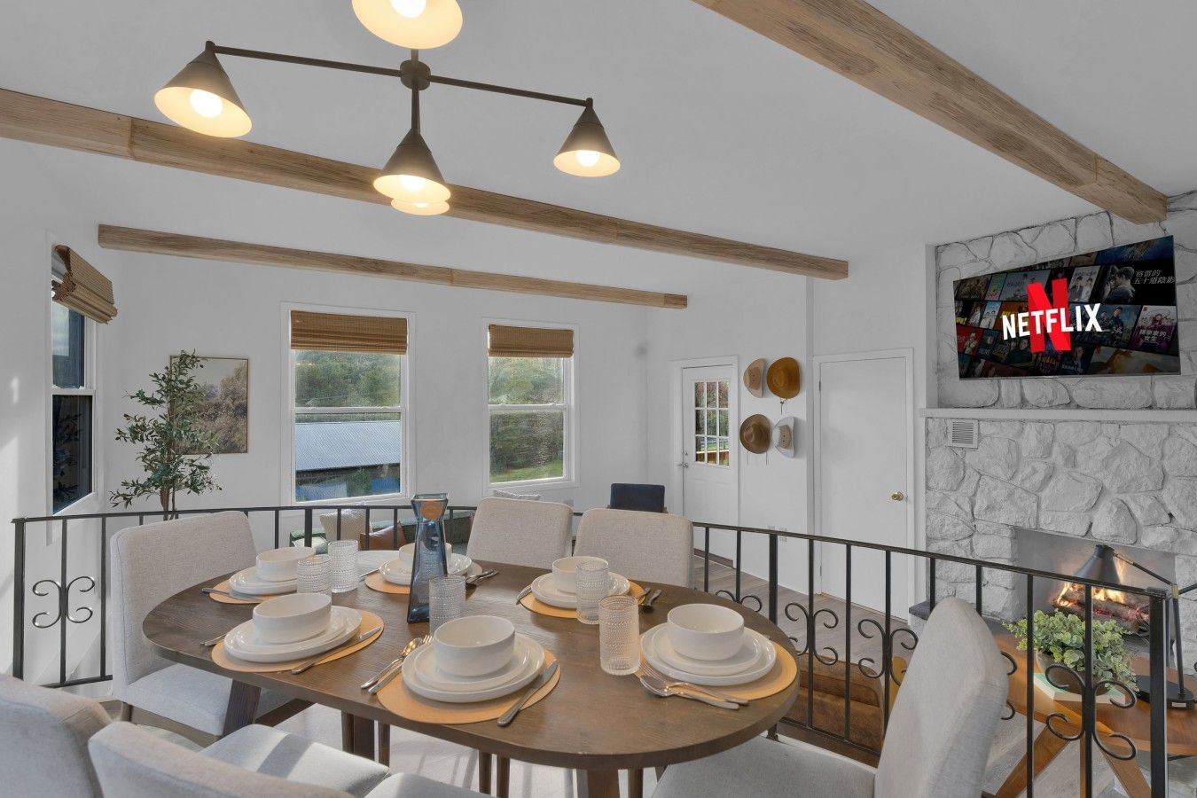 Un área de comedor con una mesa redonda dispuesta para cuatro personas, una chimenea de piedra y un televisor de pared mostrando el logotipo de Netflix.