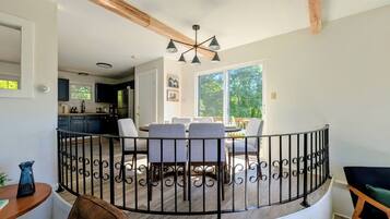 A dining area with a round table and chairs, a black metal railing, and a view of the kitchen and outdoors.