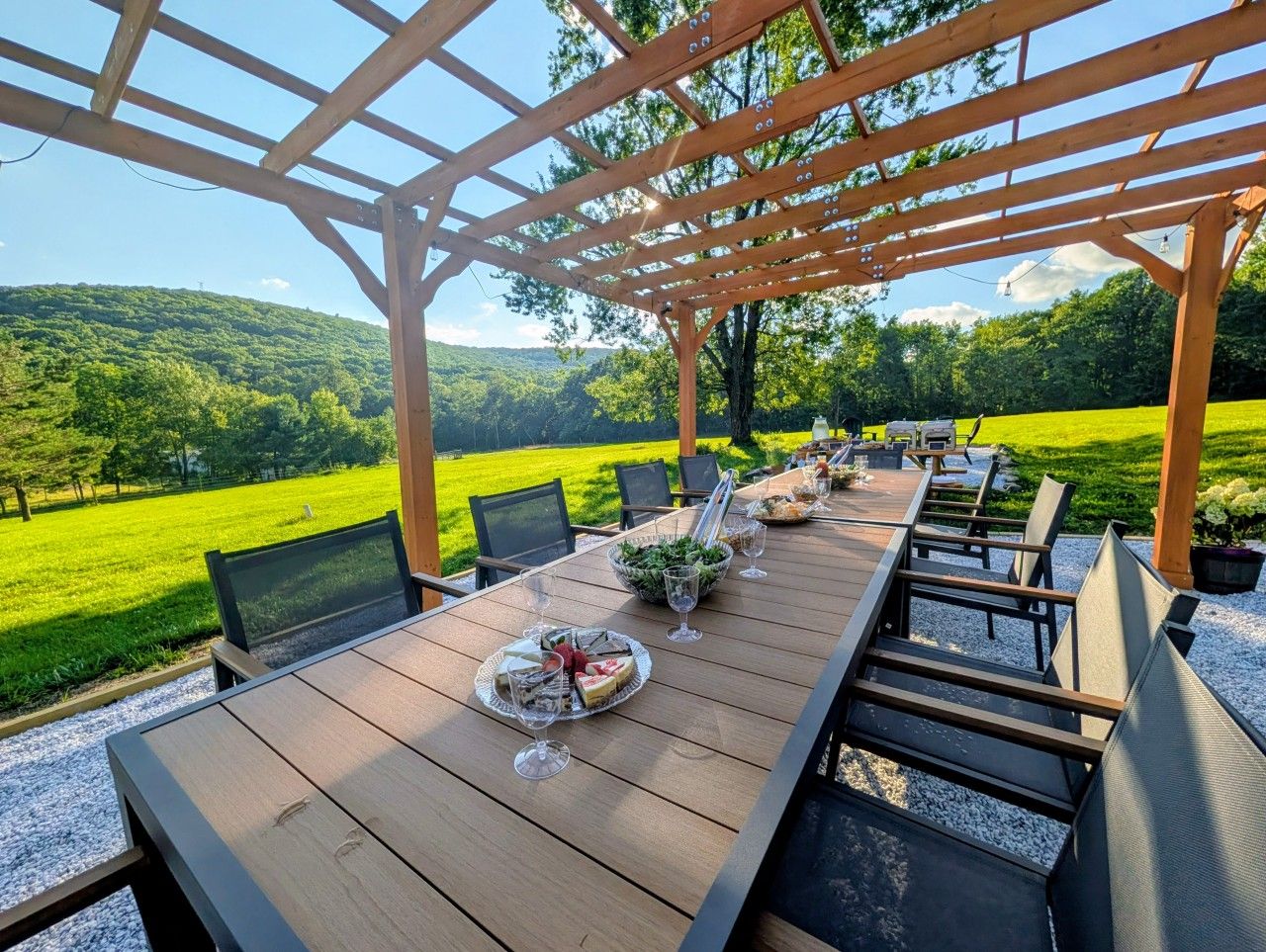 Un espacio para comer al aire libre con una pérgola, una larga mesa de madera y sillas.