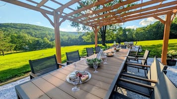 Un espacio para comer al aire libre con una pérgola, una larga mesa de madera y sillas.