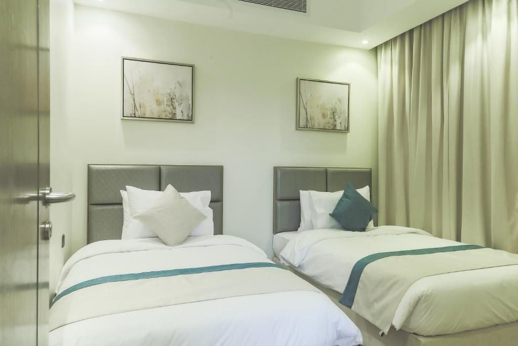 Une chambre d’hôtel avec deux lits, chacun doté d’une tête de lit, de draps blancs et d’un élément décoratif de couleur turquoise.