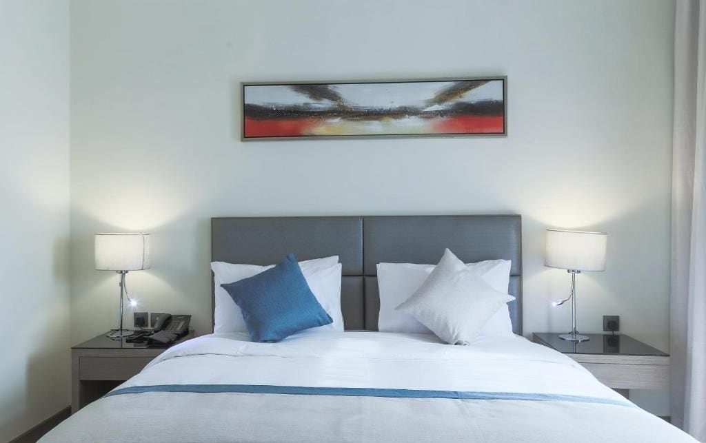 Una habitación de hotel con una cama grande, dos mesitas de noche, un teléfono y un cuadro en la pared.