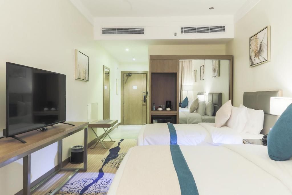 A hotel room with a television, a bed, a desk, and a wardrobe.