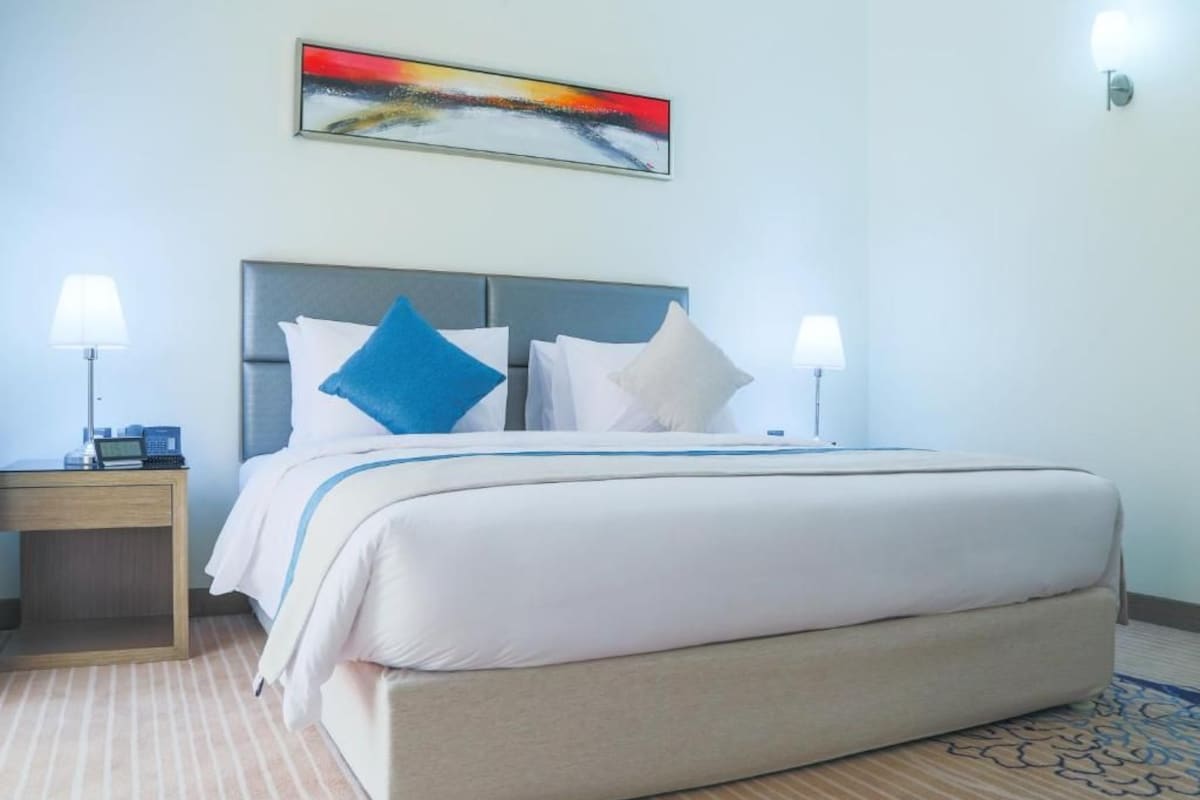 A hotel room with a bed, two bedside tables, a lamp, and a painting on the wall.