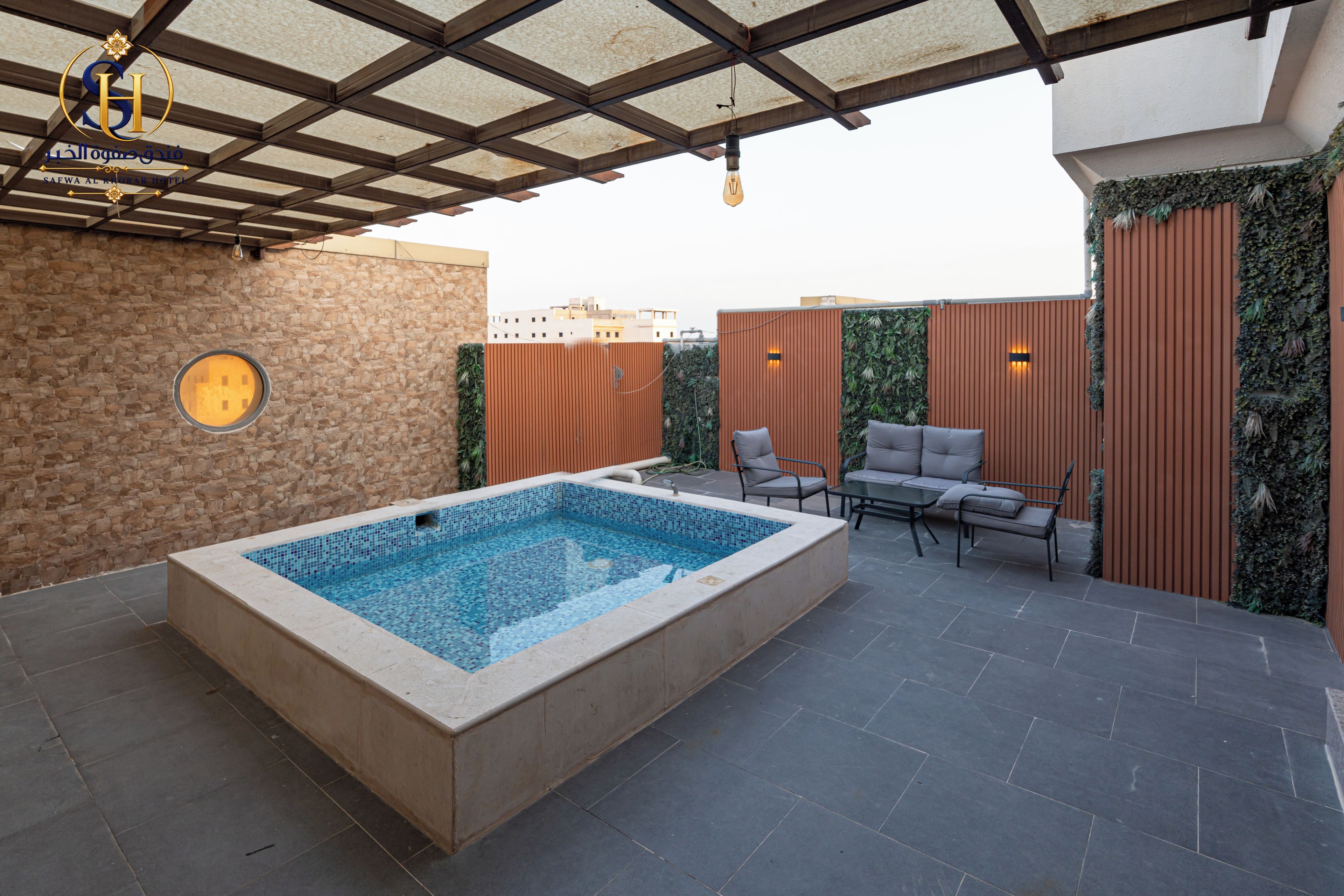 Une piscine dotée d’une terrasse carrelée, entourée de murs en pierre et agrémentée d’une pergola en bois.