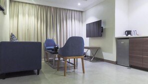 A modern hotel room with a sofa, a chair, a small table, a TV mounted on the wall, and a kitchenette area. - sfwat alkhobar hotel (Al Khobar)